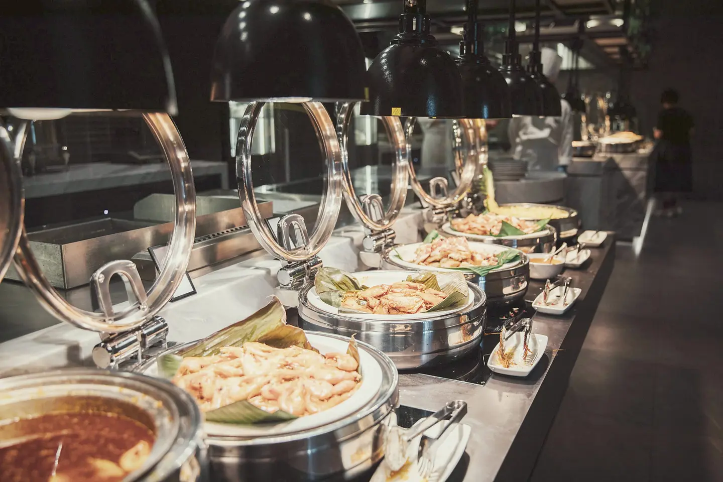Hotel-style buffet line with silver chafing dishes under heat lamps